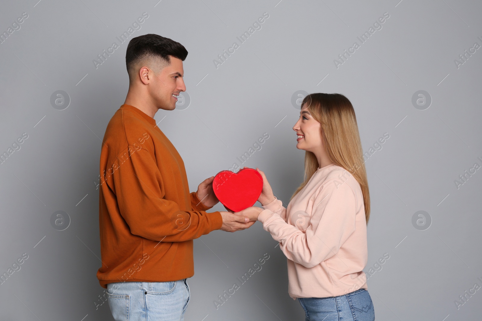 Photo of Man surprising his girlfriend with gift on grey background. Valentine's day celebration