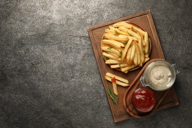 Delicious french fries served with sauces on grey textured table, top view. Space for text