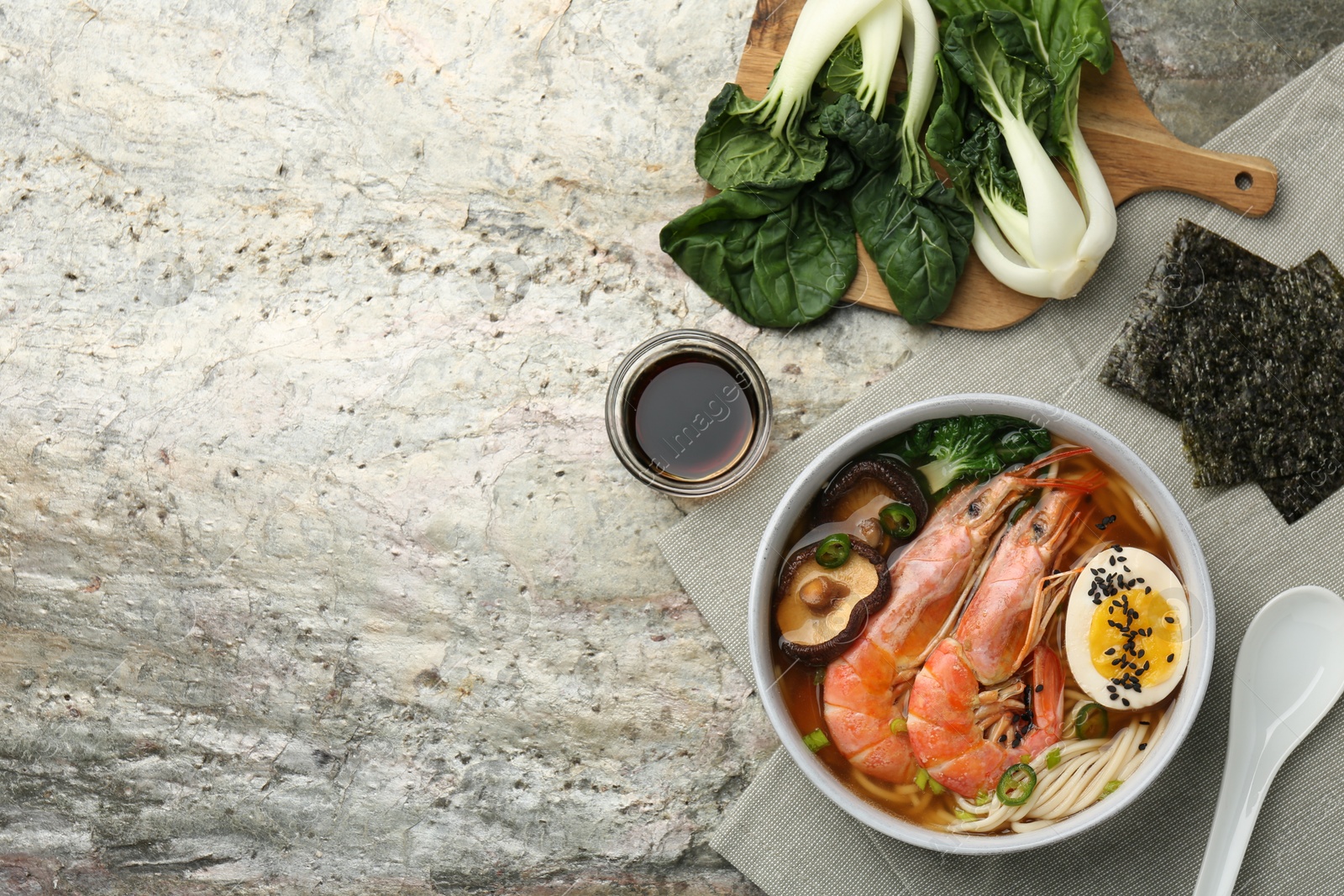 Photo of Delicious ramen with shrimps and egg in bowl served on grey textured table, flat lay with space for text. Noodle soup