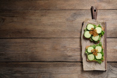 Photo of Tasty cucumber sandwiches with arugula and mustard on wooden table, top view. Space for text