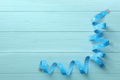 Measuring tape on light blue wooden table, top view. Space for text