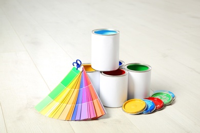 Photo of Cans of paint and color palette on wooden floor indoors