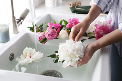 Woman with beautiful peonies near kitchen sink, closeup