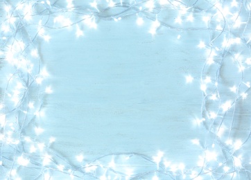 Photo of Frame made with Christmas lights on light wooden background, top view. Space for text