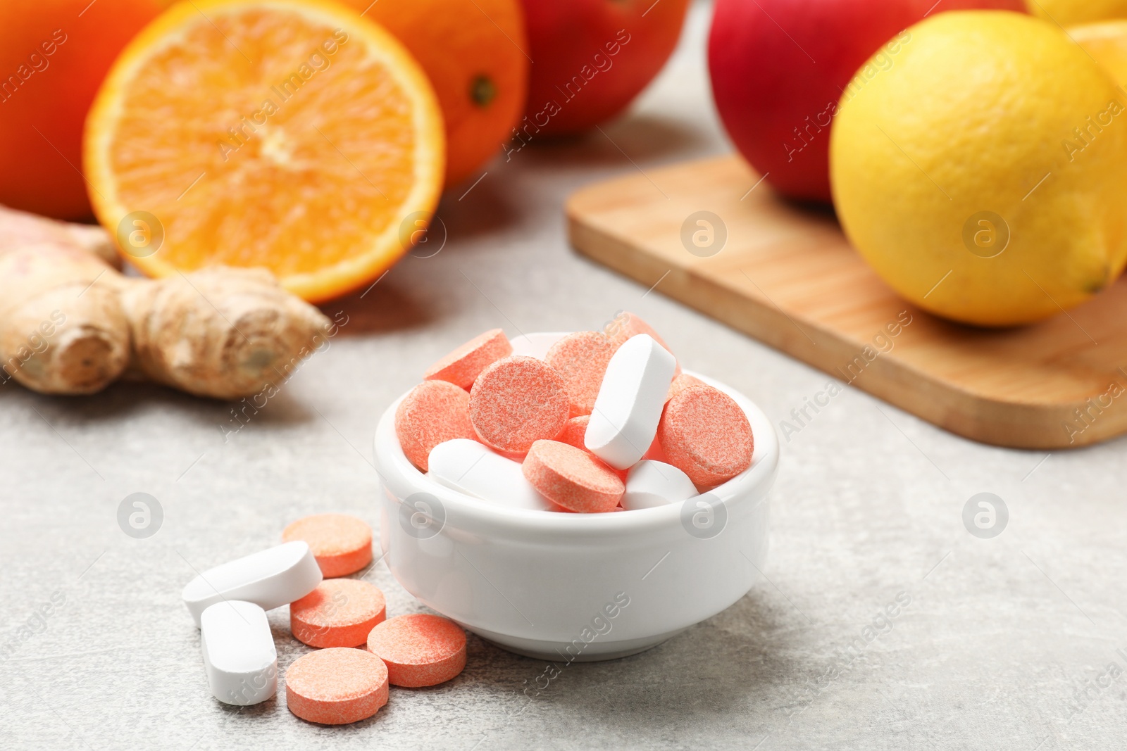 Photo of Dietary supplements. Different pills in bowl, fruits and ginger on grey table