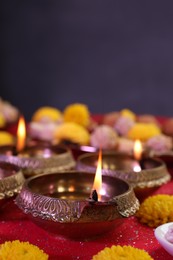 Photo of Diwali celebration. Diya lamps and chrysanthemum flowers on shiny red table, closeup