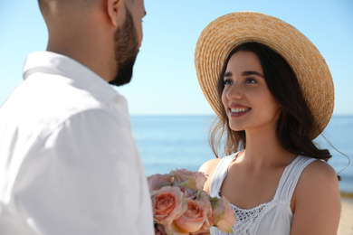 Photo of Happy young couple with flowers at beach near sea. Honeymoon trip