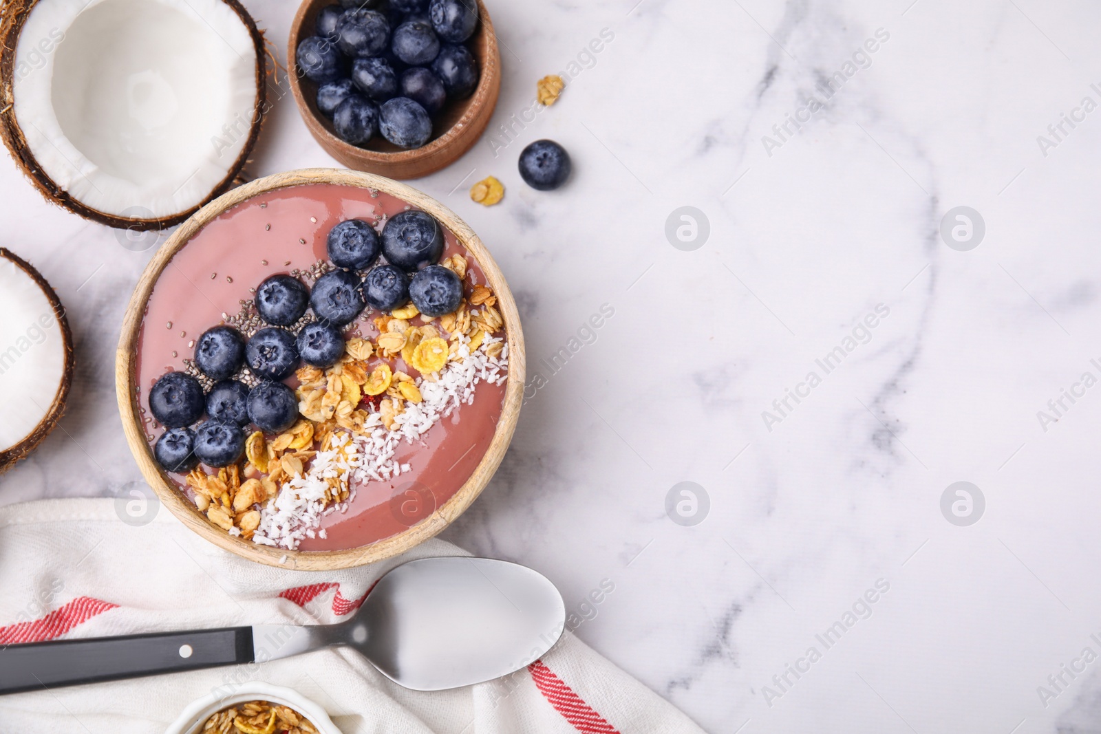 Photo of Bowl of delicious fruit smoothie served with fresh blueberries, granola and coconut flakes on white marble table, flat lay. Space for text