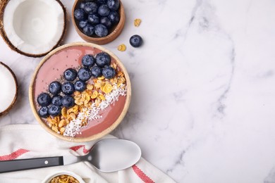 Bowl of delicious fruit smoothie served with fresh blueberries, granola and coconut flakes on white marble table, flat lay. Space for text