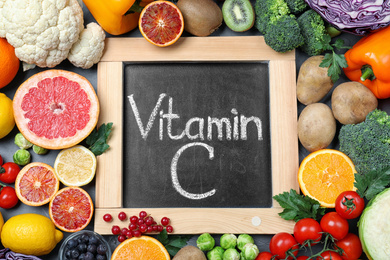 Photo of Different products and blackboard with phrase VITAMIN C on table