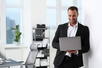 Photo of Smiling young businessman using laptop in office. Space for text