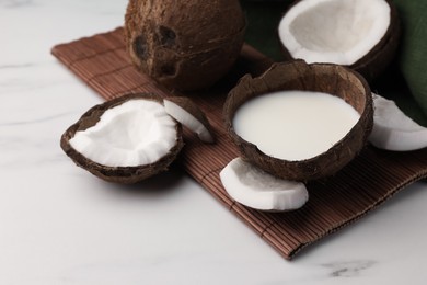 Delicious vegan milk in coconut and pieces of ripe fruit on white table, closeup