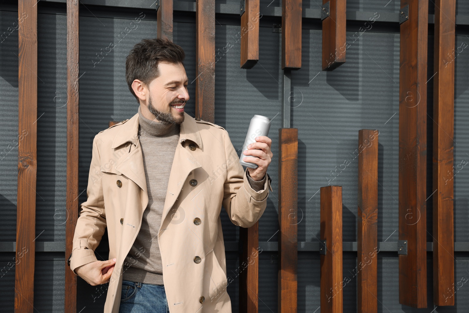 Photo of Happy man holding tin can with beverage outdoors. Space for text