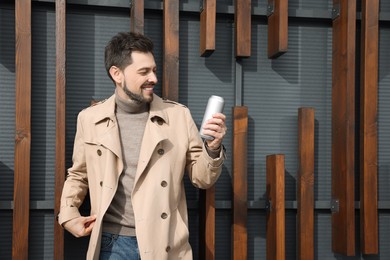 Photo of Happy man holding tin can with beverage outdoors. Space for text