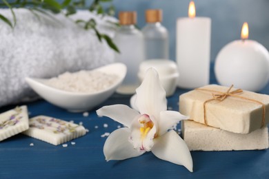 Photo of Soap bars and beautiful flower on blue wooden table, closeup with space for text. Retreat concept
