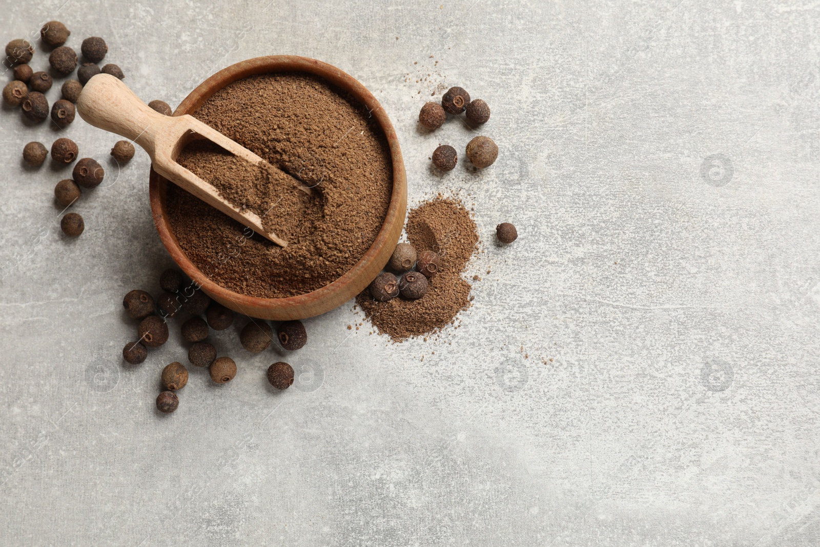 Photo of Ground allspice pepper in bowl, grains and scoop on grey table, flat lay. Space for text