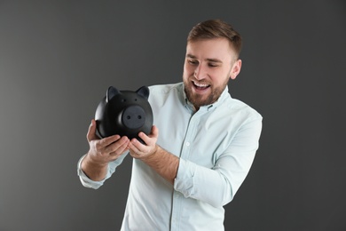 Portrait of happy young man with piggy bank on grey background. Money saving