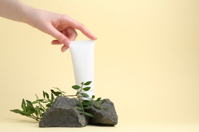 Photo of Woman with tube of cream, branches and stones on light yellow background, closeup