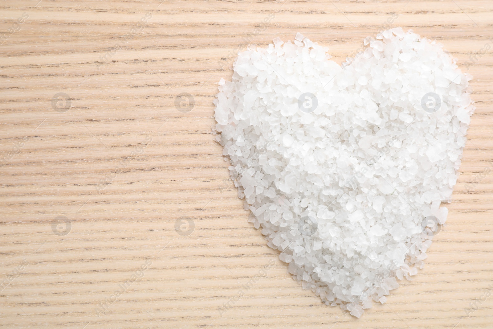 Photo of Heart made of white sea salt on wooden background, top view with space for text. Spa treatment