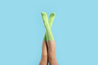 Photo of Woman in stylish lime socks on light blue background, closeup