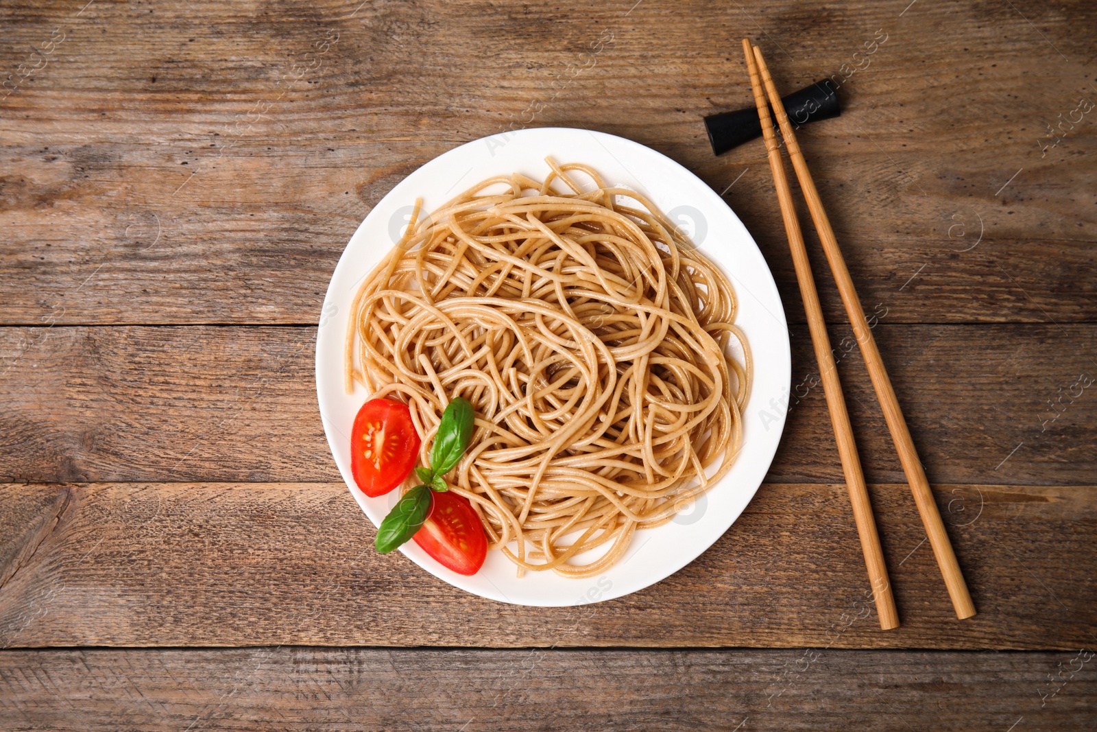 Photo of Tasty buckwheat noodles with chopsticks on wooden table, flat lay