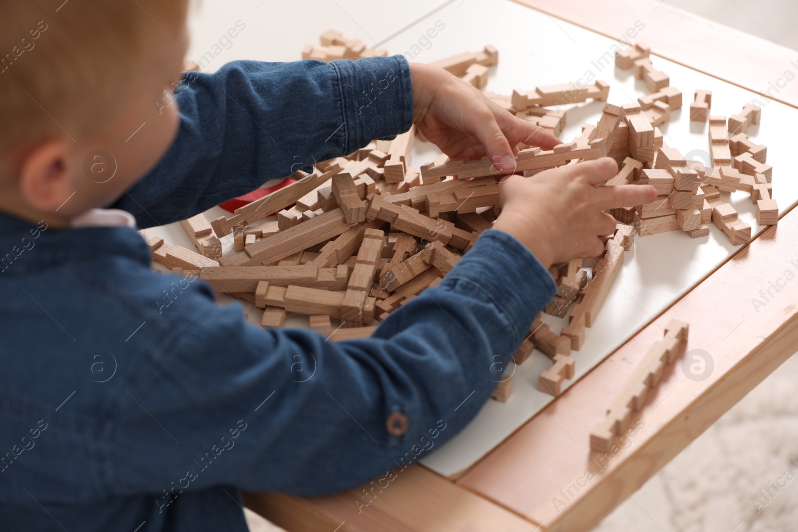 Photo of Little boy playing with wooden blocks at table indoors, closeup. Child's toy