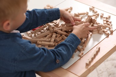 Little boy playing with wooden blocks at table indoors, closeup. Child's toy