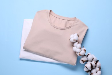 Cotton branch with fluffy flowers and t-shirts on light blue background, top view