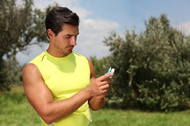Young man checking pulse with medical device after training in park. Space for text