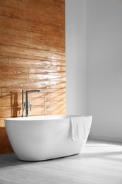 Photo of White bathtub with towel near wooden wall in room