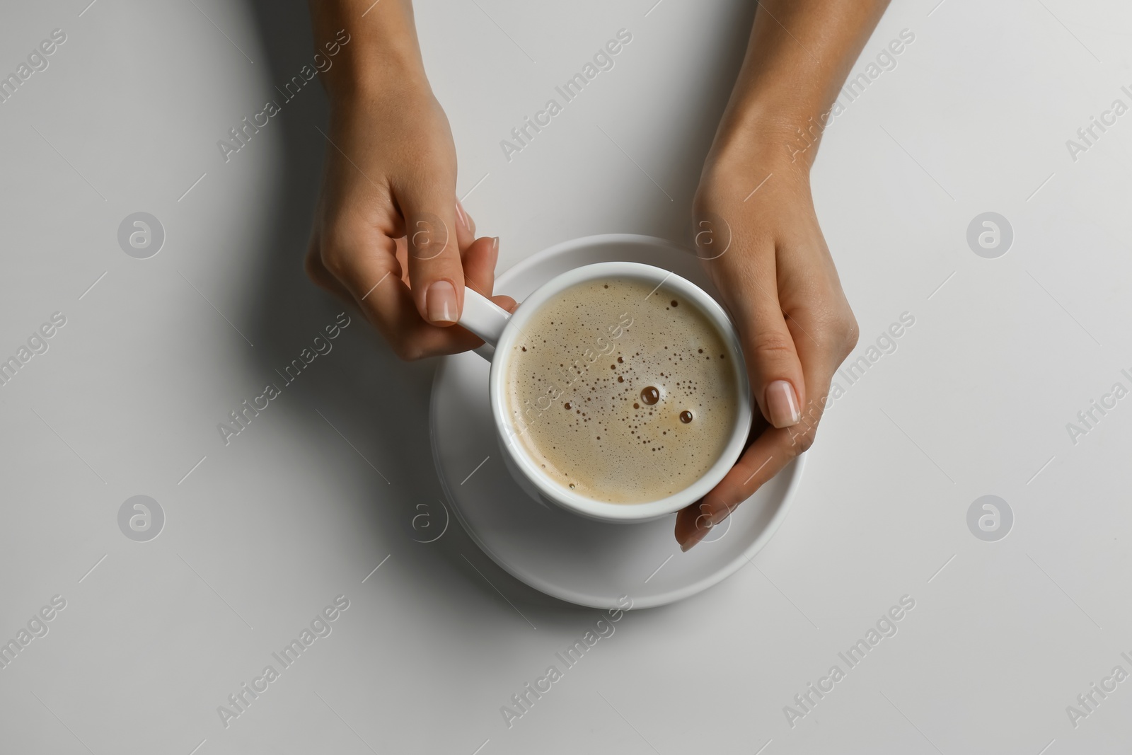 Photo of Woman holding cup of coffee at white table, top view