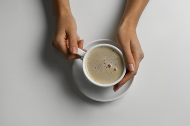 Photo of Woman holding cup of coffee at white table, top view