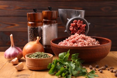 Photo of Manual meat grinder with beef mince, spices and parsley on wooden table