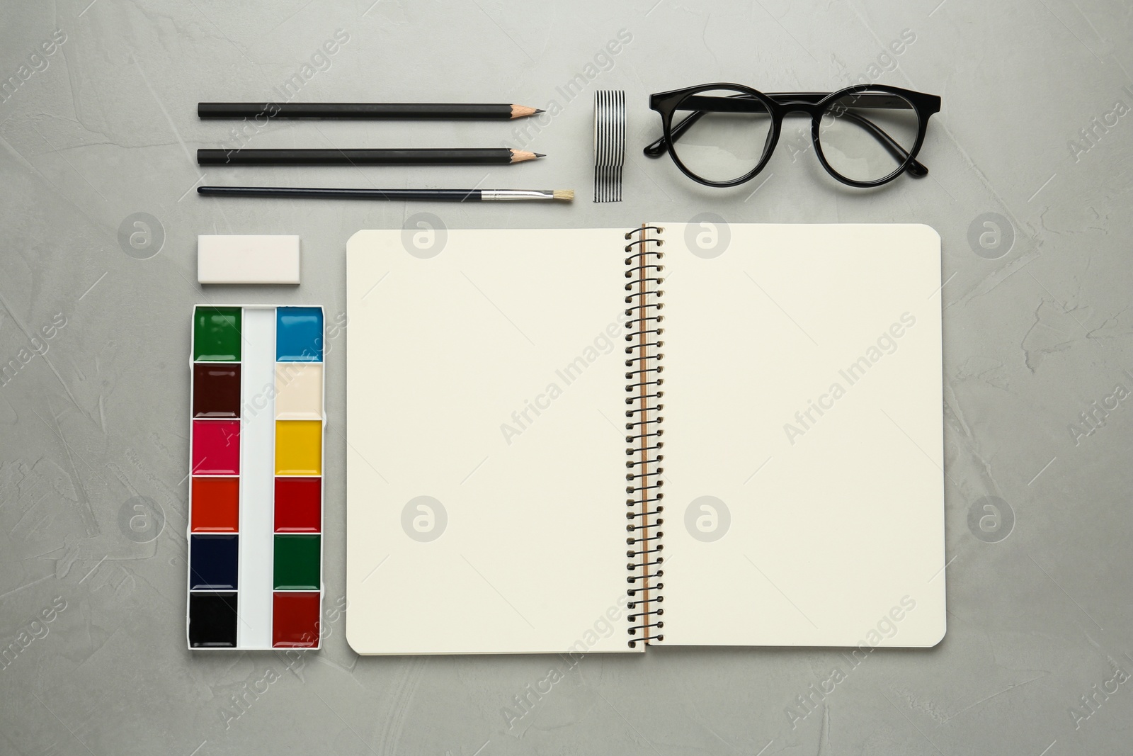 Photo of Flat lay composition with blank sketchbook on light grey stone table. Space for text