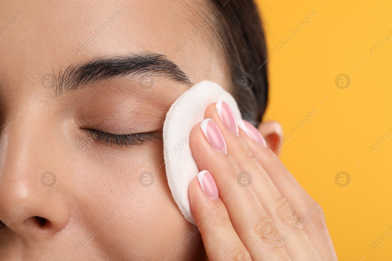 Photo of Beautiful woman removing makeup with cotton pad on orange background, closeup. Space for text