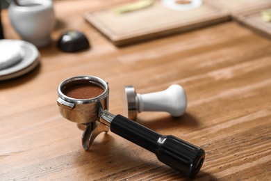 Photo of Portafilter with milled coffee and tamper on wooden table, closeup. Space for text