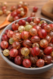 Bowl full of ripe gooseberries on wooden table, closeup