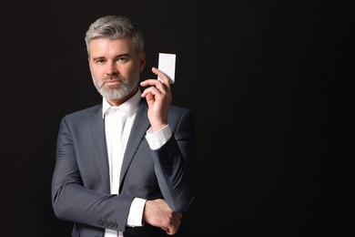 Handsome businessman holding blank business card on black background. Space for text