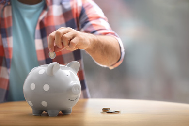 Photo of Man putting money into piggy bank at table, closeup. Space for text