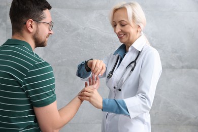 Doctor checking patient's pulse during consultation near grey wall