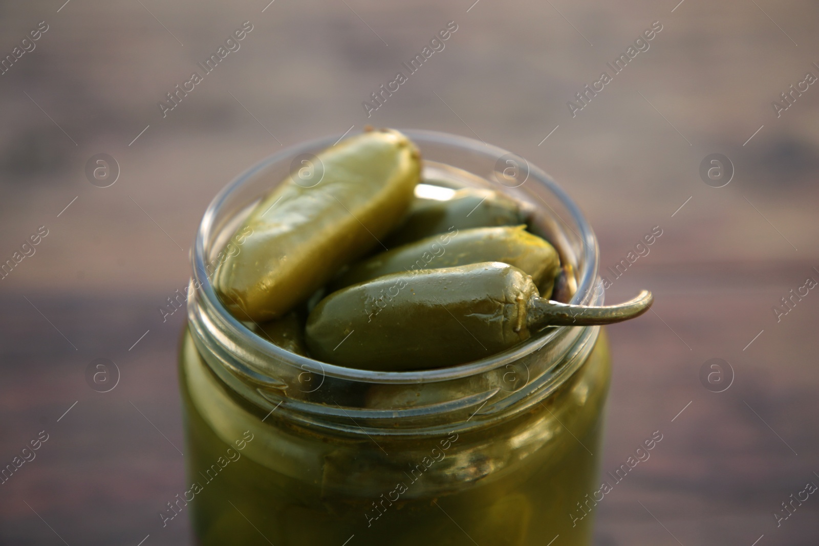 Photo of Glass jar of pickled green jalapeno peppers on wooden table, closeup