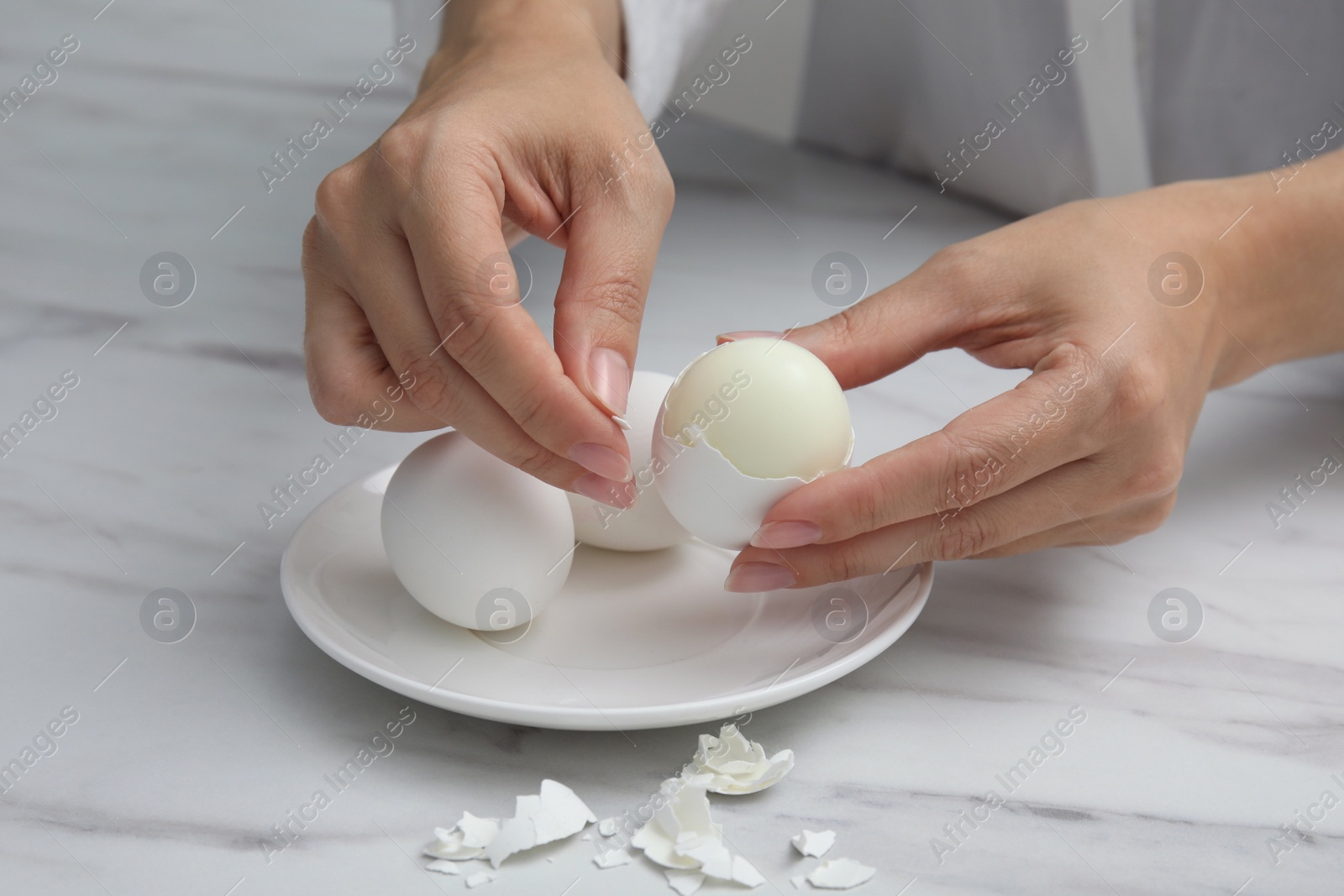 Photo of Woman peeling boiled egg at white marble table, closeup