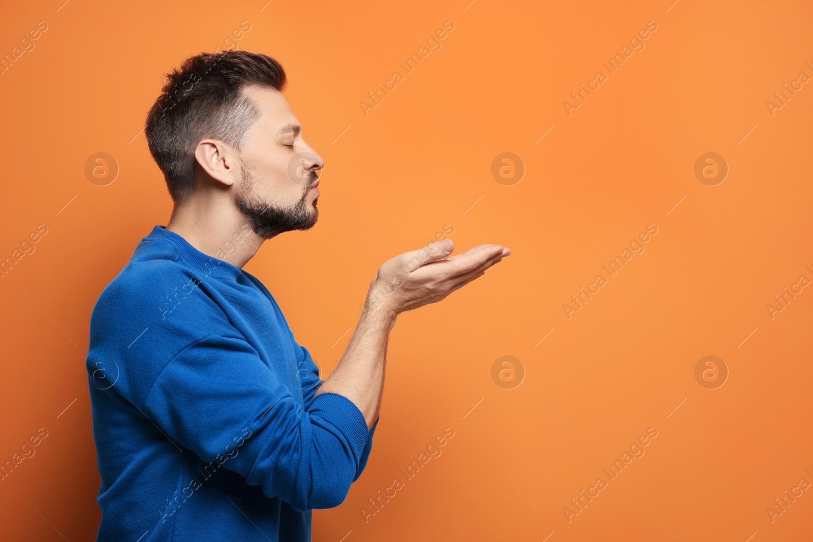 Photo of Handsome man blowing kiss on orange background. Space for text