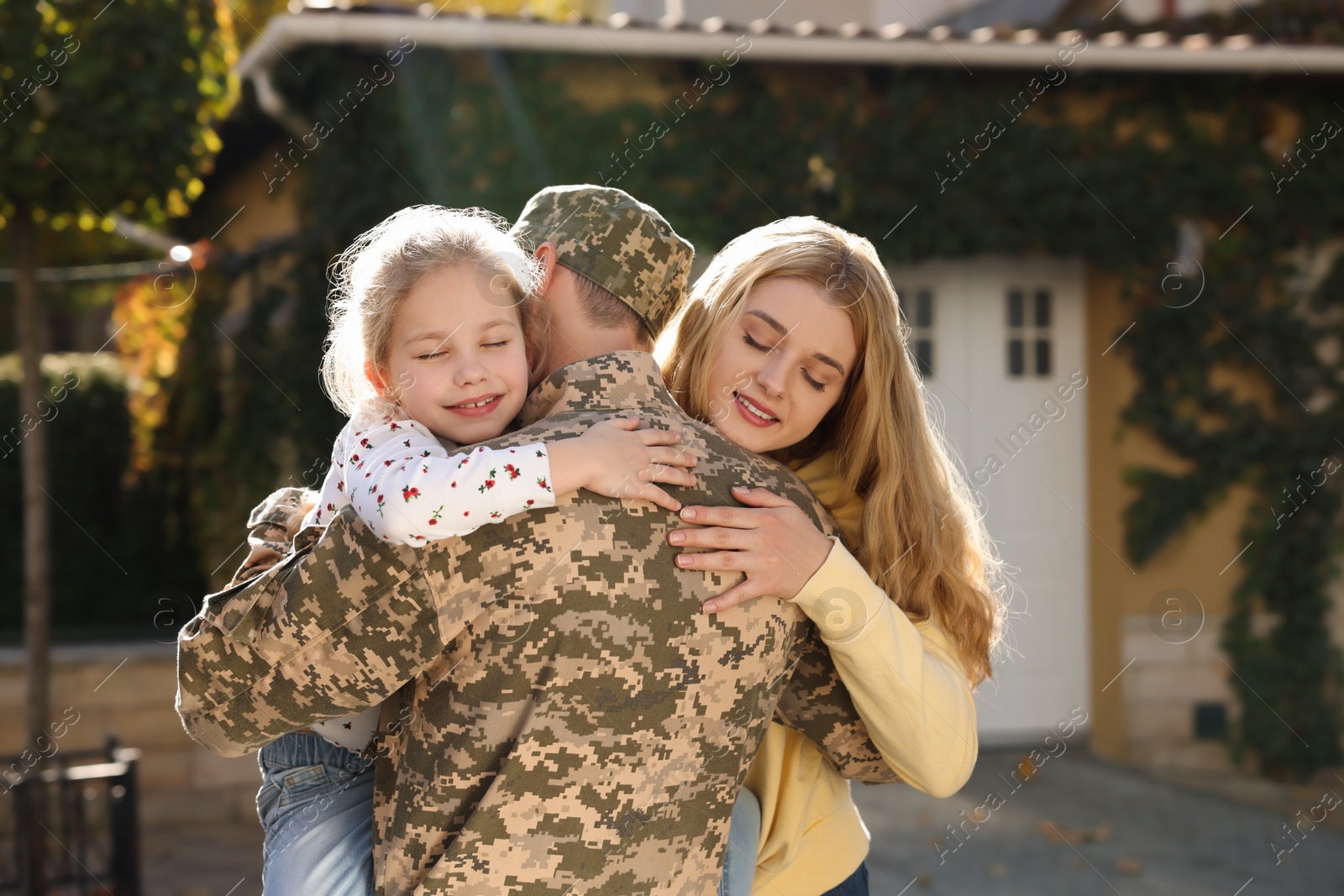 Photo of Daughter and wife hugging soldier in Ukrainian military uniform outdoors. Family reunion