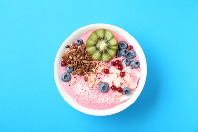 Photo of Tasty smoothie bowl with fresh kiwi fruit, berries and granola on light blue background, top view