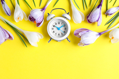 Photo of White alarm clock with spring flowers and space for text on yellow background, flat lay. Time change