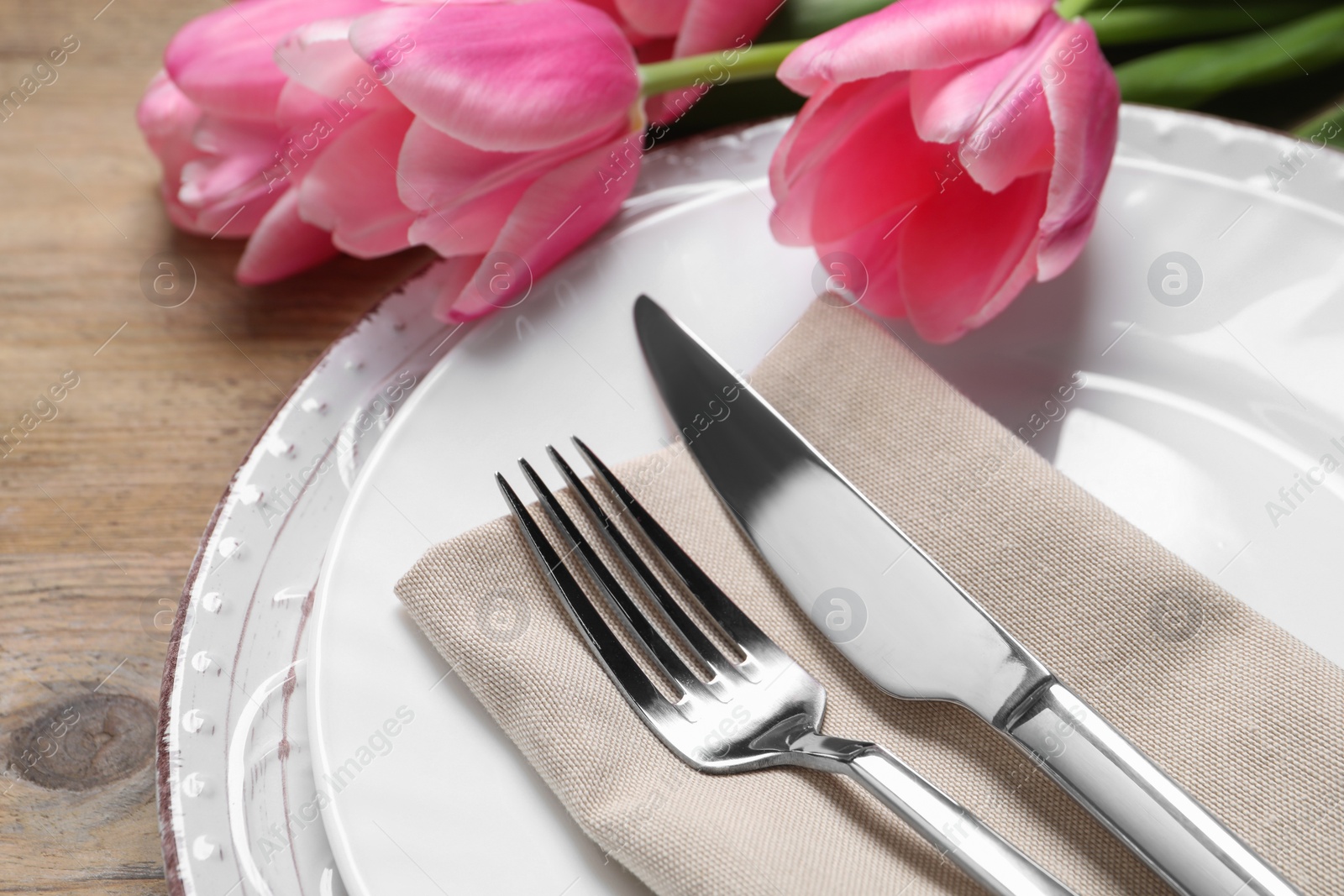 Photo of Stylish table setting with cutlery and tulips on wooden background, closeup