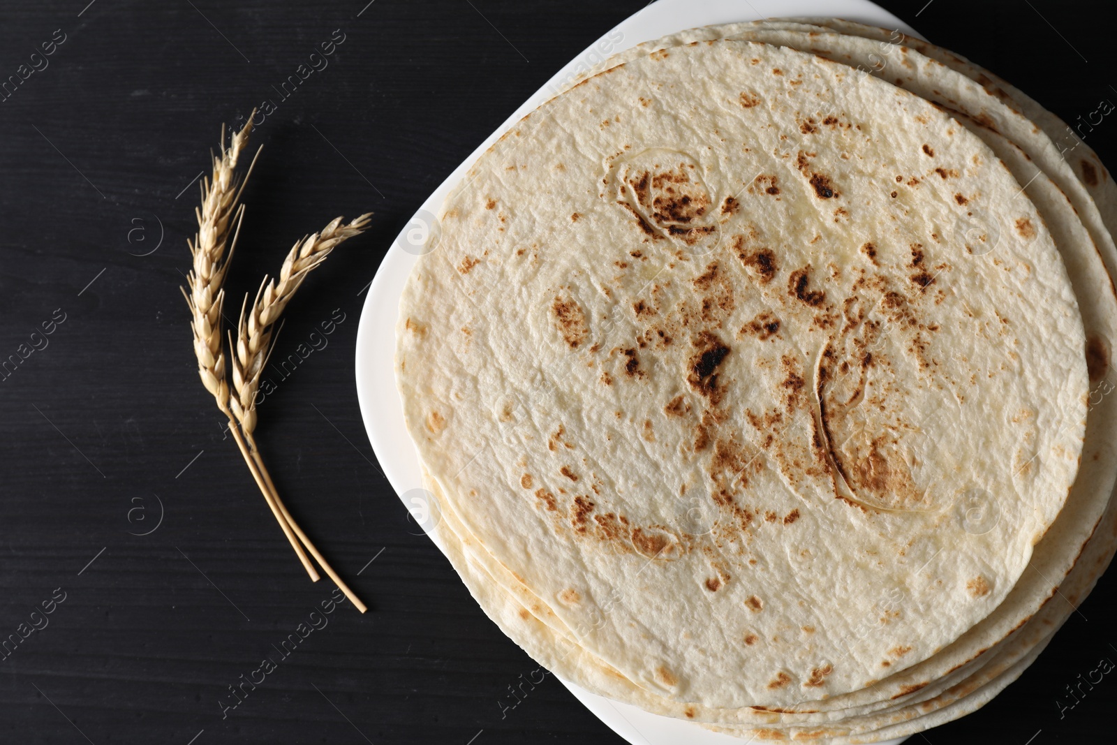 Photo of Many tasty homemade tortillas on black wooden table, top view