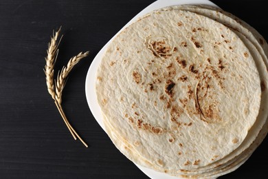 Many tasty homemade tortillas on black wooden table, top view