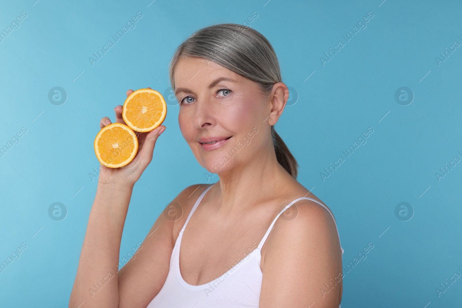 Photo of Beautiful woman with halves of orange rich in vitamin C on light blue background